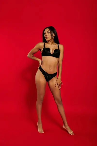 A young Black woman in stylish lingerie poses confidently against a bold red backdrop. — Stock Photo