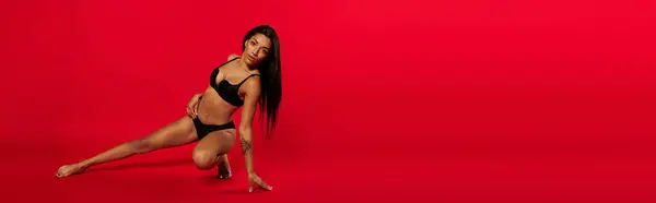 A confident young Black woman poses in black lingerie against a red studio backdrop, banner — Stock Photo