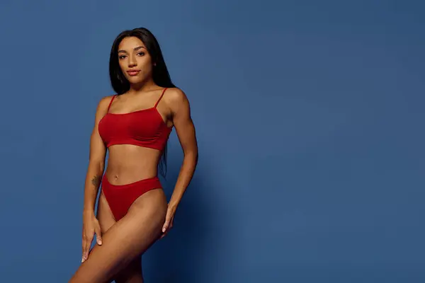 A stunning young Black woman in red lingerie poses confidently against a vibrant blue backdrop. — Stock Photo