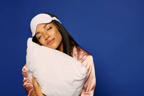 A young african american woman with brunette hair relaxes with a pillow, wearing silk pajamas. — Stock Photo