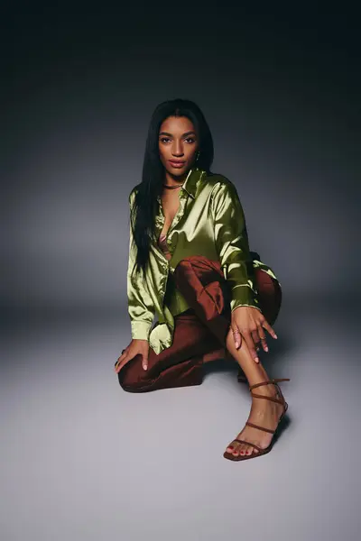 A beautiful young woman showcases her elegance in a green silk shirt while striking a pose. — Stock Photo