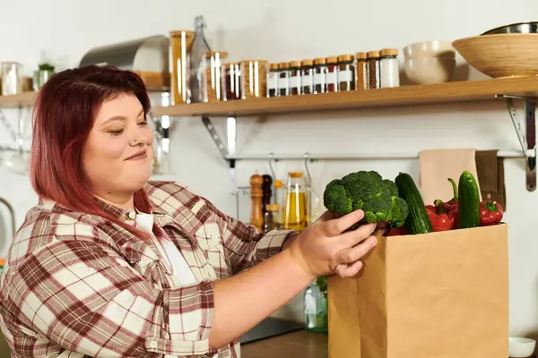 Mujer joven sonríe mientras explora cuidadosamente una caja de productos frescos en su cocina vibrante. - foto de stock