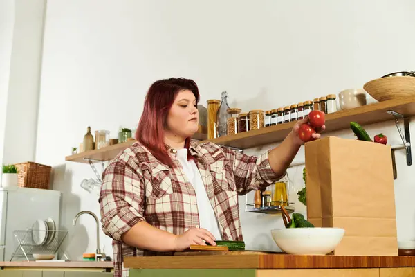 Молода жінка плюс розмір організовує свіжі продукти на дерев'яній стійці на яскравій кухні. — стокове фото