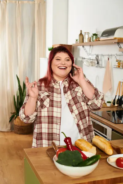 Un allegro plus size donna chatta al telefono mentre prepara ingredienti freschi in cucina. — Foto stock