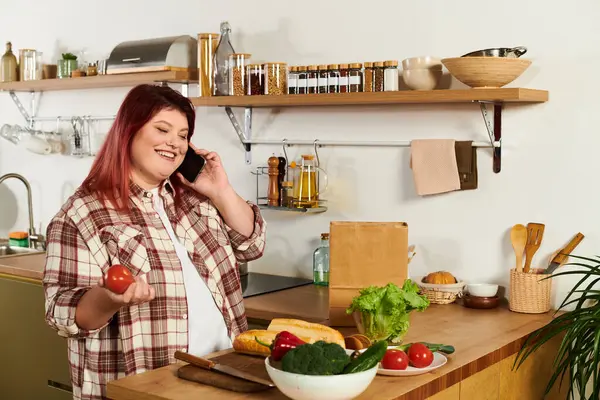 Young woman enjoys preparing food while talking on her phone in a cozy kitchen space. — Stock Photo