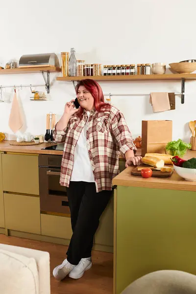 Яркая и привлекательная кухня с молодой женщиной plus size, счастливо разговаривающей по телефону. — стоковое фото
