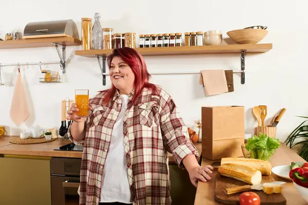 Young woman with vibrant red hair smiles while holding a drink in her stylish kitchen. — Stock Photo