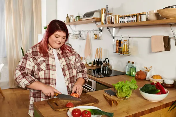 A young plus size woman cuts vegetables on a wooden board in a bright kitchen while cooking. — Stock Photo