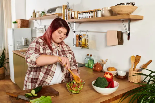 A young plus size woman mixes fresh vegetables in a bowl while enjoying her kitchen space. — Stock Photo