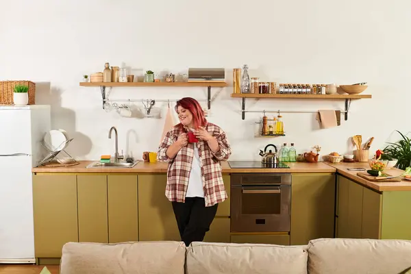 A young plus size woman smiles while holding a drink in her stylish kitchen filled with decor. — Stock Photo