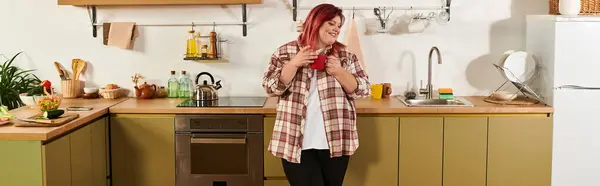 A cheerful plus size woman relaxes in a colorful kitchen while savoring a refreshing drink. — Stock Photo