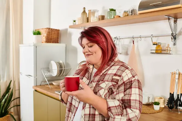 Joyful woman holds a red cup while savoring a warm drink in her stylish kitchen space. — Stock Photo