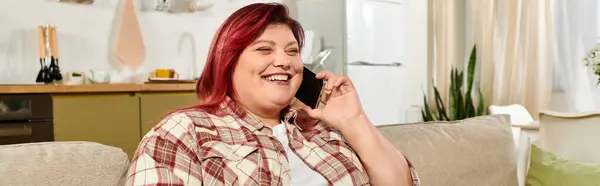 Young woman with vibrant hair laughs on the phone in a bright, inviting living room. — Stock Photo