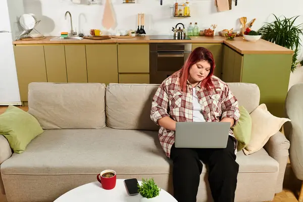 Young plus size woman sits on a couch, focused on her laptop while relaxing indoors — Stock Photo