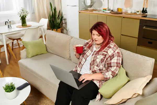 Молодая женщина plus size наслаждается кофе, сосредоточившись на работе в стильном жилом пространстве. — стоковое фото