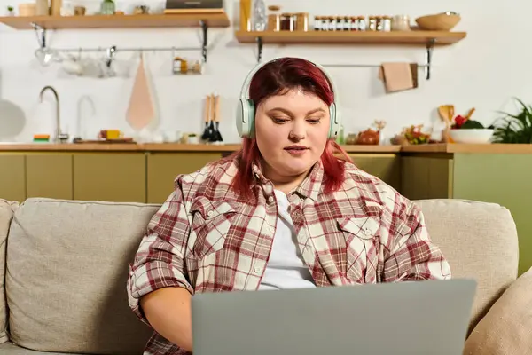 Bright living space features a young plus size woman enjoying a laptop session with headphones on — Stock Photo