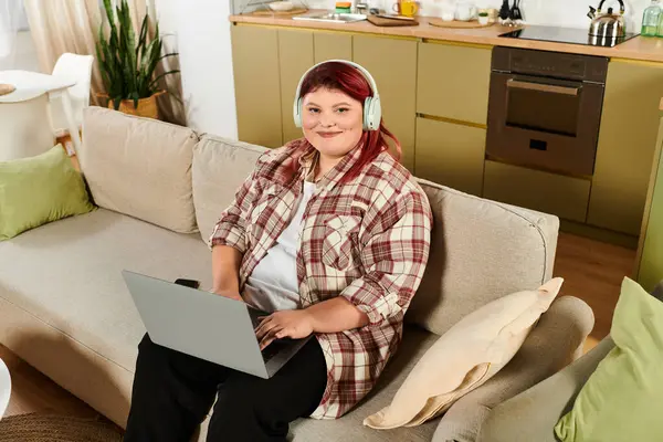 Young woman engages with laptop in stylish living space while wearing headphones and smiling — Stock Photo