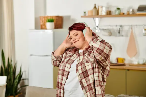 Женщина plus size любит музыку в наушниках, чувствуя себя расслабленной на стильной кухне. — стоковое фото