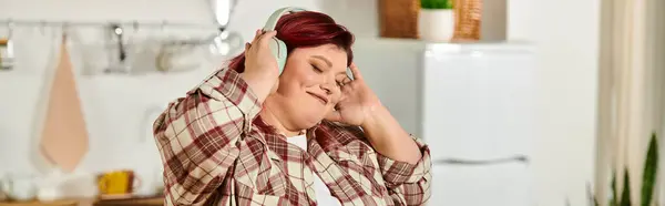 Женщина plus size с удовольствием слушает музыку, готовя еду на светлой кухне — стоковое фото