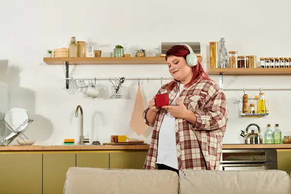 A young plus size woman savors her drink while listening to music in a stylish kitchen. — Stock Photo