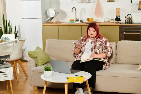 A plus size woman sits on a stylish sofa with a notebook and phone, embracing creativity. — Stock Photo