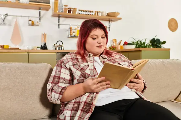 A plus size woman enjoys a peaceful moment absorbed in a book on her couch. — Stock Photo