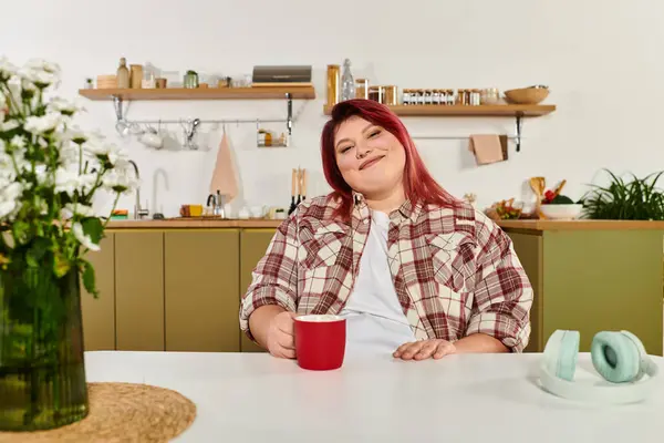 Молодая женщина plus size наслаждается своим временем на яркой кухне, потягивая теплый напиток. — стоковое фото