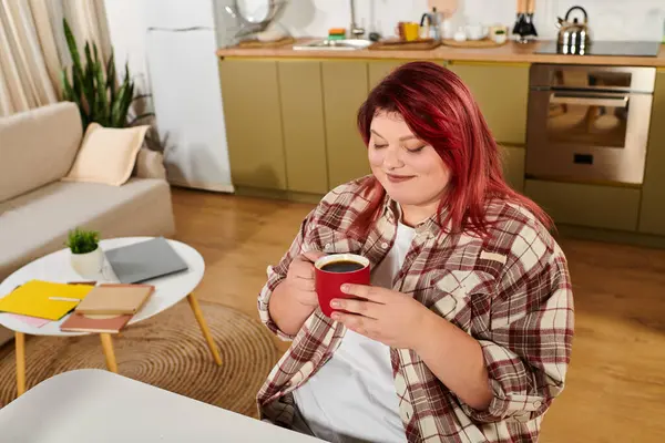 A young plus size woman savors her coffee while relaxing in a modern kitchen. — Stock Photo