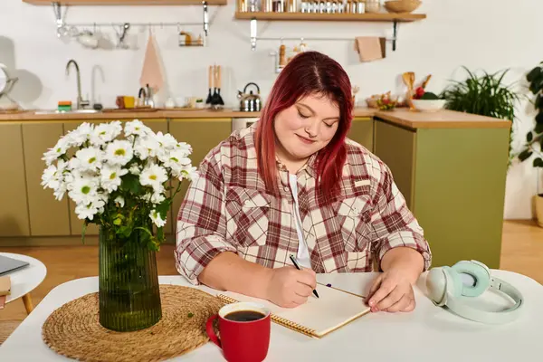 Smiling plus size woman writes in her notebook, surrounded by flowers and a warm coffee cup. — Stock Photo