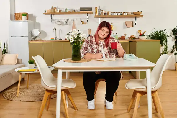 A lovely plus size woman enjoys tea and journaling in her modern kitchen. — Stock Photo