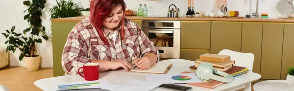 Plus size woman smiles while sketching ideas at a cozy kitchen table surrounded by inspiration. — Stock Photo