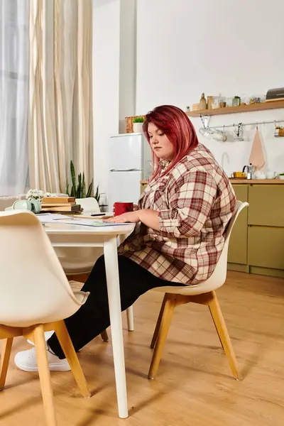 Una joven mujer de talla grande se dedica a un trabajo creativo en su mesa de comedor rodeada de plantas. - foto de stock