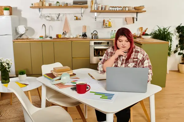 Young woman engages with her laptop while surrounded by books and plants in a bright kitchen. — Stock Photo