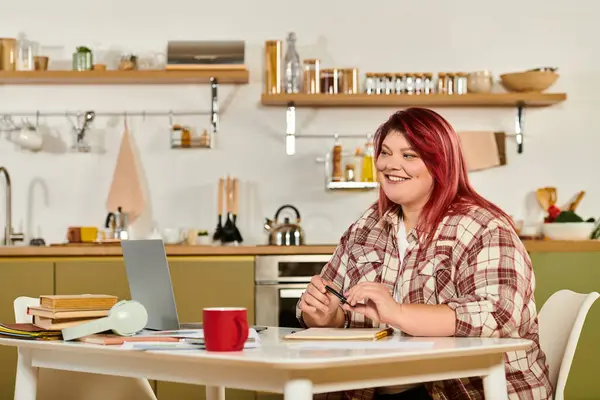 Beautiful plus size woman smiles while working at her desk in a stylish kitchen atmosphere. — Stock Photo