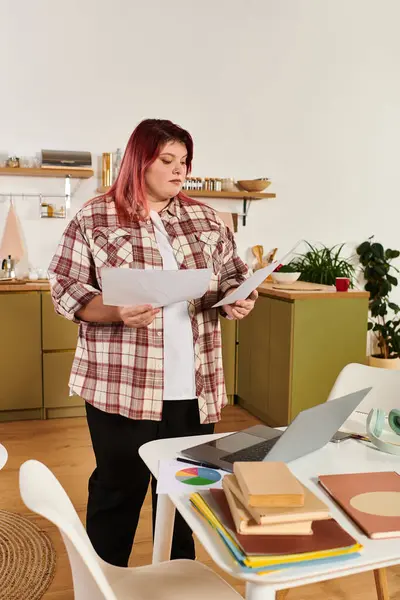 Una joven mujer de talla grande se encuentra en una cocina elegante, enfocada en organizar su papeleo. - foto de stock