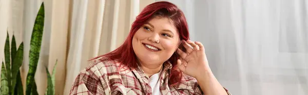 Женщина plus size с рыжими волосами наслаждается своей красотой, отдыхая дома с радостью. — стоковое фото