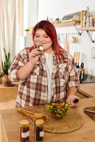 Молодая plus size женщина любит добавлять специи в свой оживленный салат в теплой атмосфере кухни. — стоковое фото