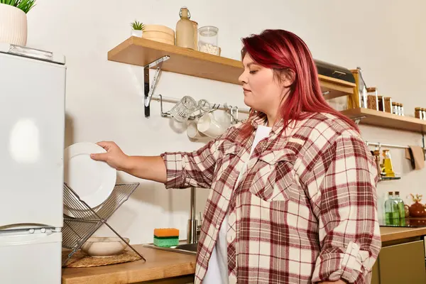Giovane donna con eleganti capelli rossi organizza piatti nella sua cucina moderna, irradiando fiducia. — Foto stock