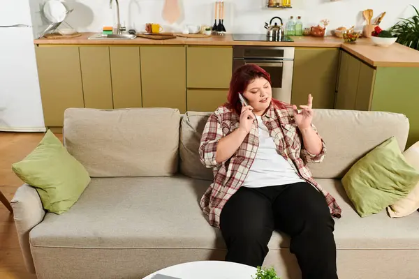 Young plus size woman enjoys a cheerful phone call while relaxing on the couch. — Stock Photo