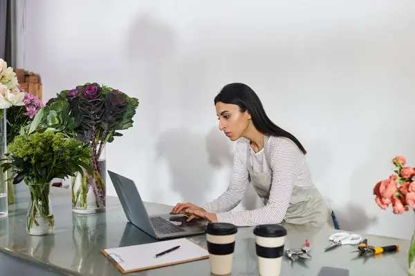 Un fleuriste dévoué travaille avec diligence sur son ordinateur portable au milieu de belles fleurs dans sa boutique. — Photo de stock