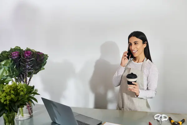 Una joven dirige su floristería, habla por teléfono y disfruta del café.. - foto de stock