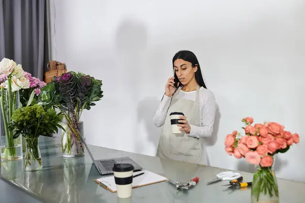 Una floristería organiza flores vibrantes mientras se comunica con un cliente por teléfono. - foto de stock