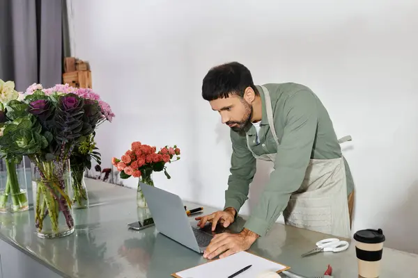 Un fleuriste habile se concentre sur son ordinateur portable au milieu d'une variété de fleurs colorées et de verdure. — Photo de stock