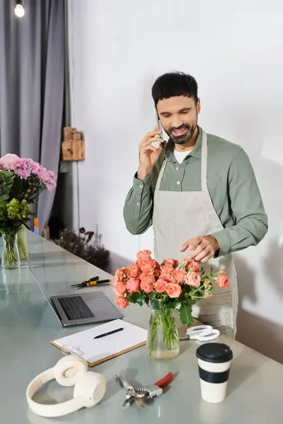 Un bel homme barbu travaille joyeusement dans sa boutique de fleurs, créant un bouquet de roses. — Photo de stock