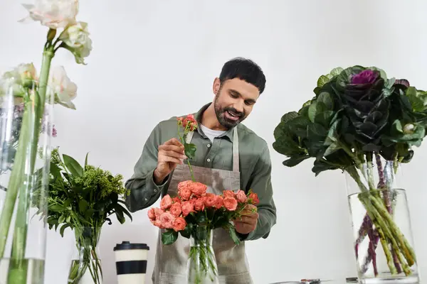 Un florista talentoso arregla expertamente hermosas rosas con una sonrisa alegre en su tienda.. - foto de stock