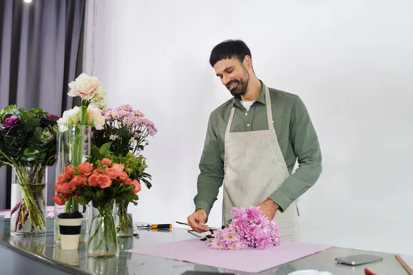 Un hombre barbudo guapo organiza un ramo en su floristería, mostrando su creatividad y pasión. - foto de stock