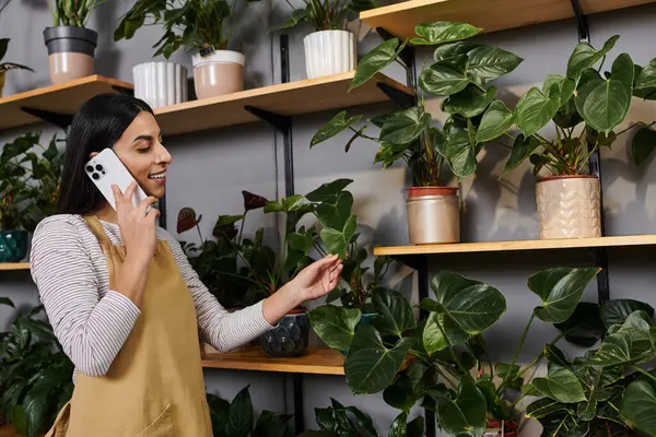 A young florist happily arranges plants while talking on the phone in her shop. — Stock Photo