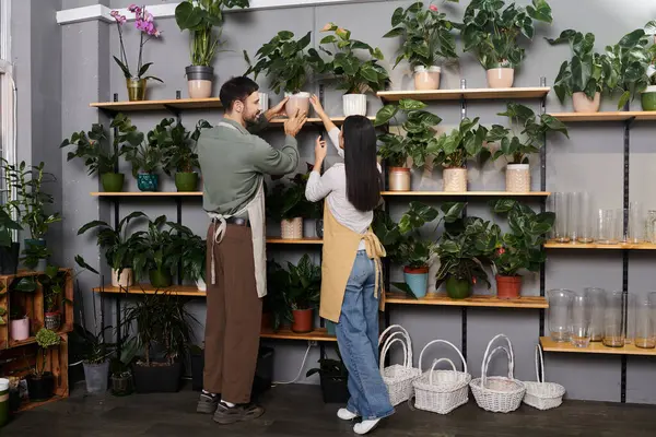 Pareja trabaja lado a lado organizando plantas y flores en su vibrante floristería. - foto de stock