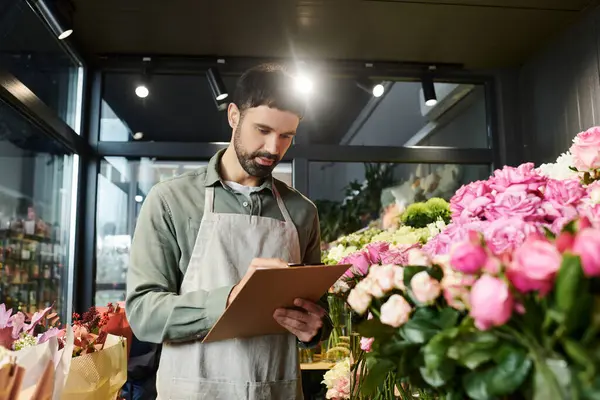 Handsome bearded man writes notes in his colorful flower shop, surrounded by blooming flora. — Stock Photo