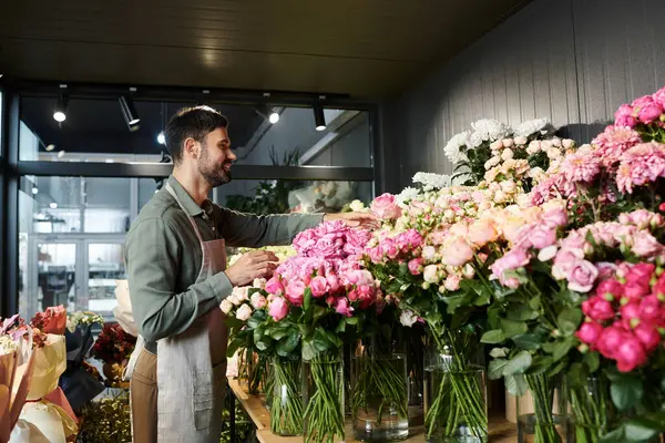 Un bell'uomo barbuto organizza fiori freschi nel suo negozio accogliente, in mostra fioriture vivaci. — Foto stock